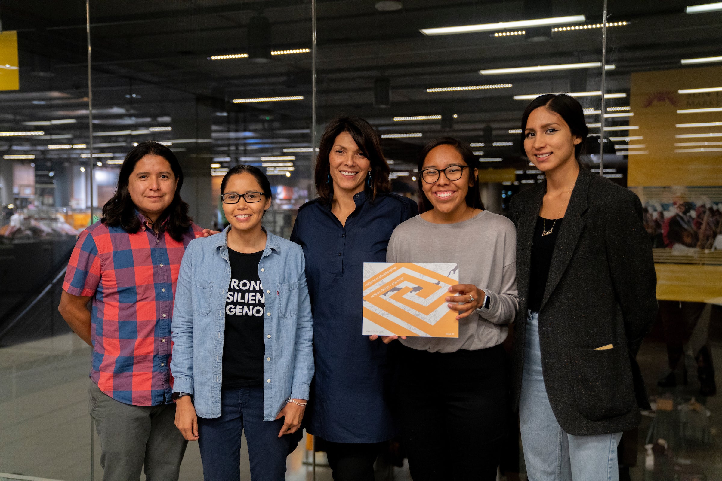 professor with group of students, one of who is holding a book