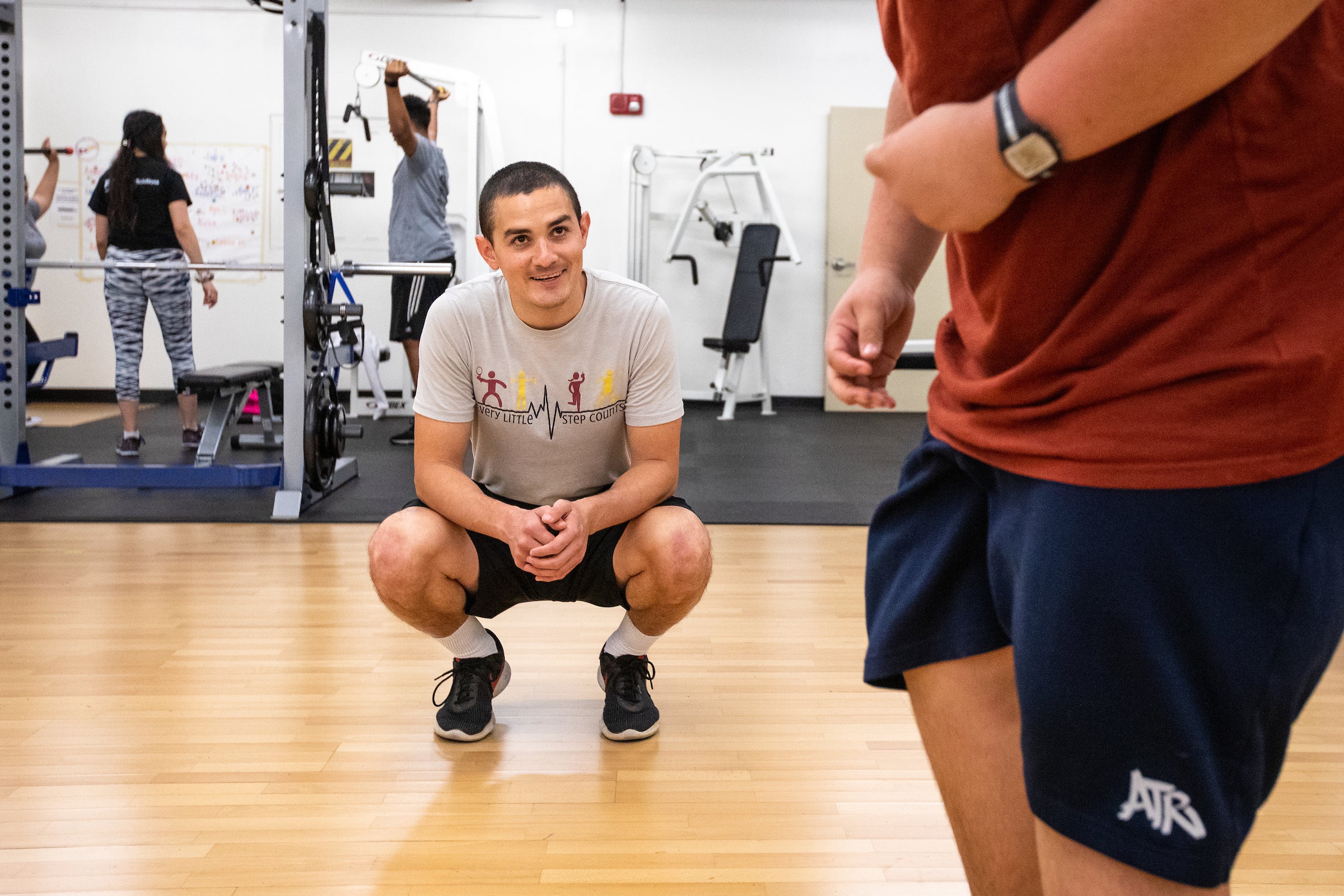 man crouching in a gym watching as torso of person in foreground jogs past