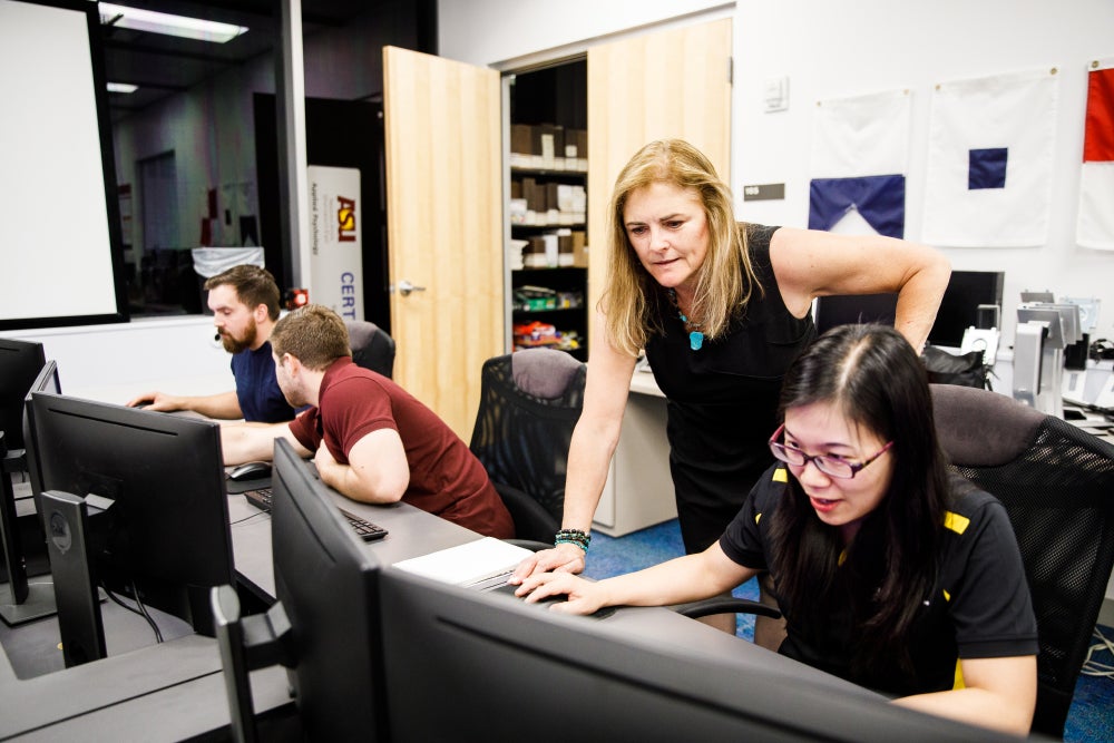 Cooke stands behind student at computer during a class