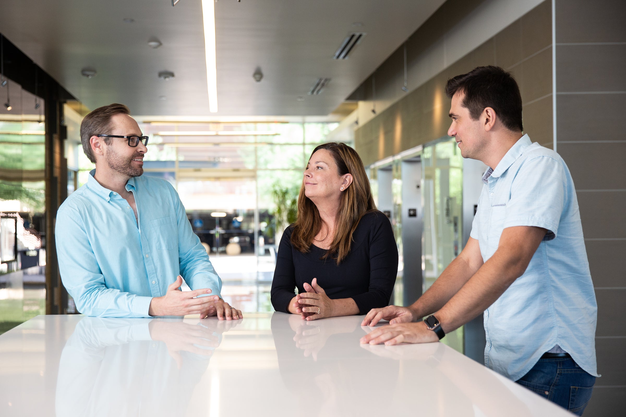 two men and a woman stand at a table, talking