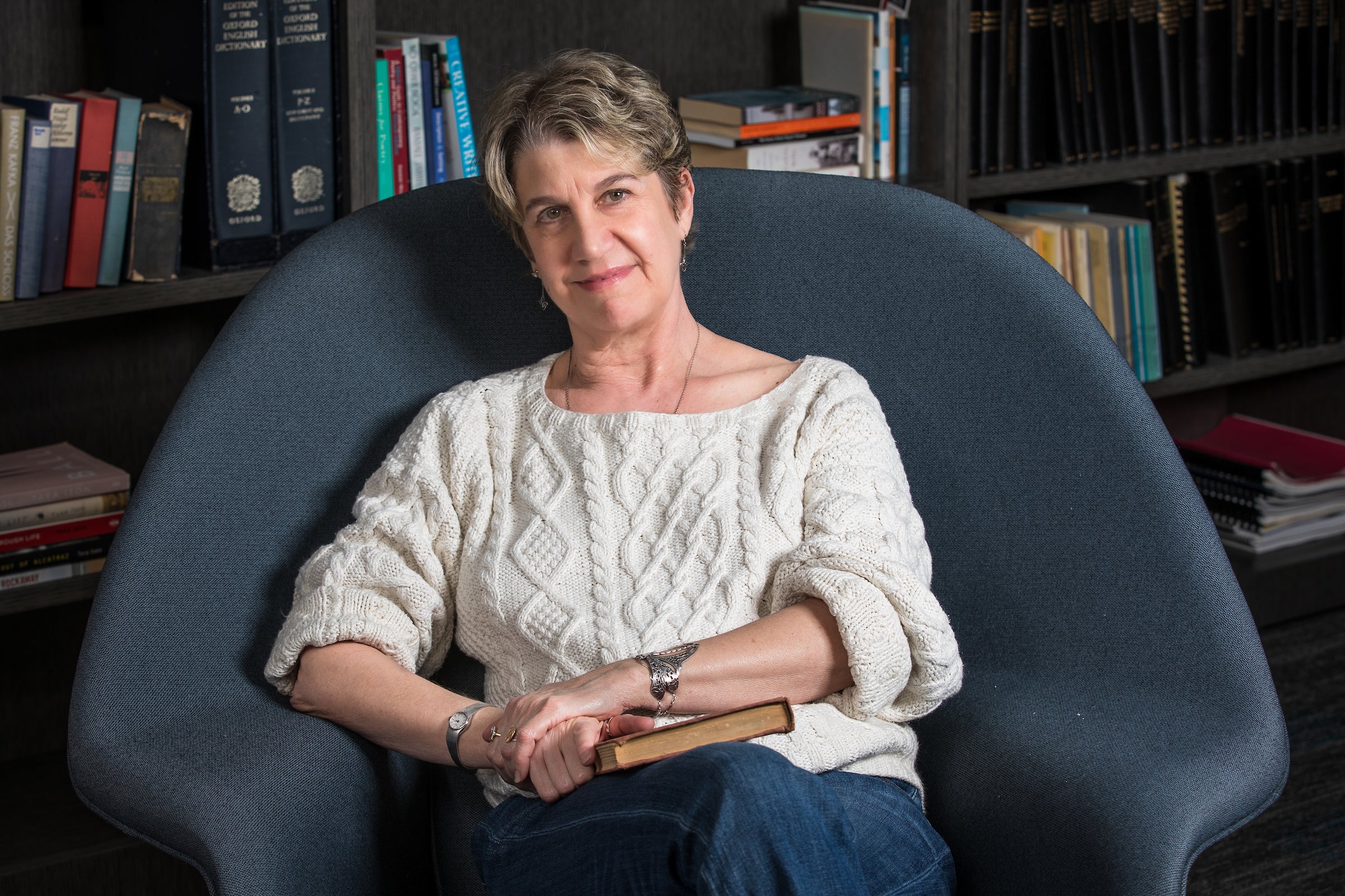 Tara Ison sits in a chair in front of shelves of books