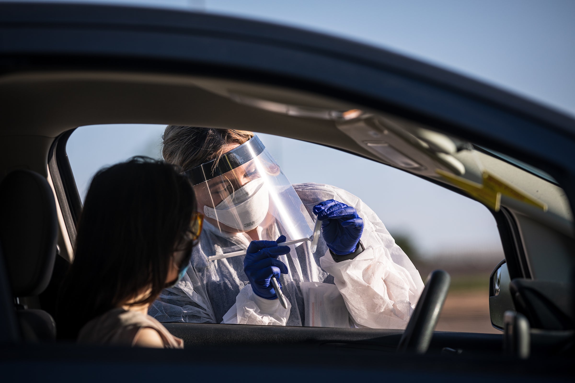 A COVID testing volunteer gives instructions to someone in a car