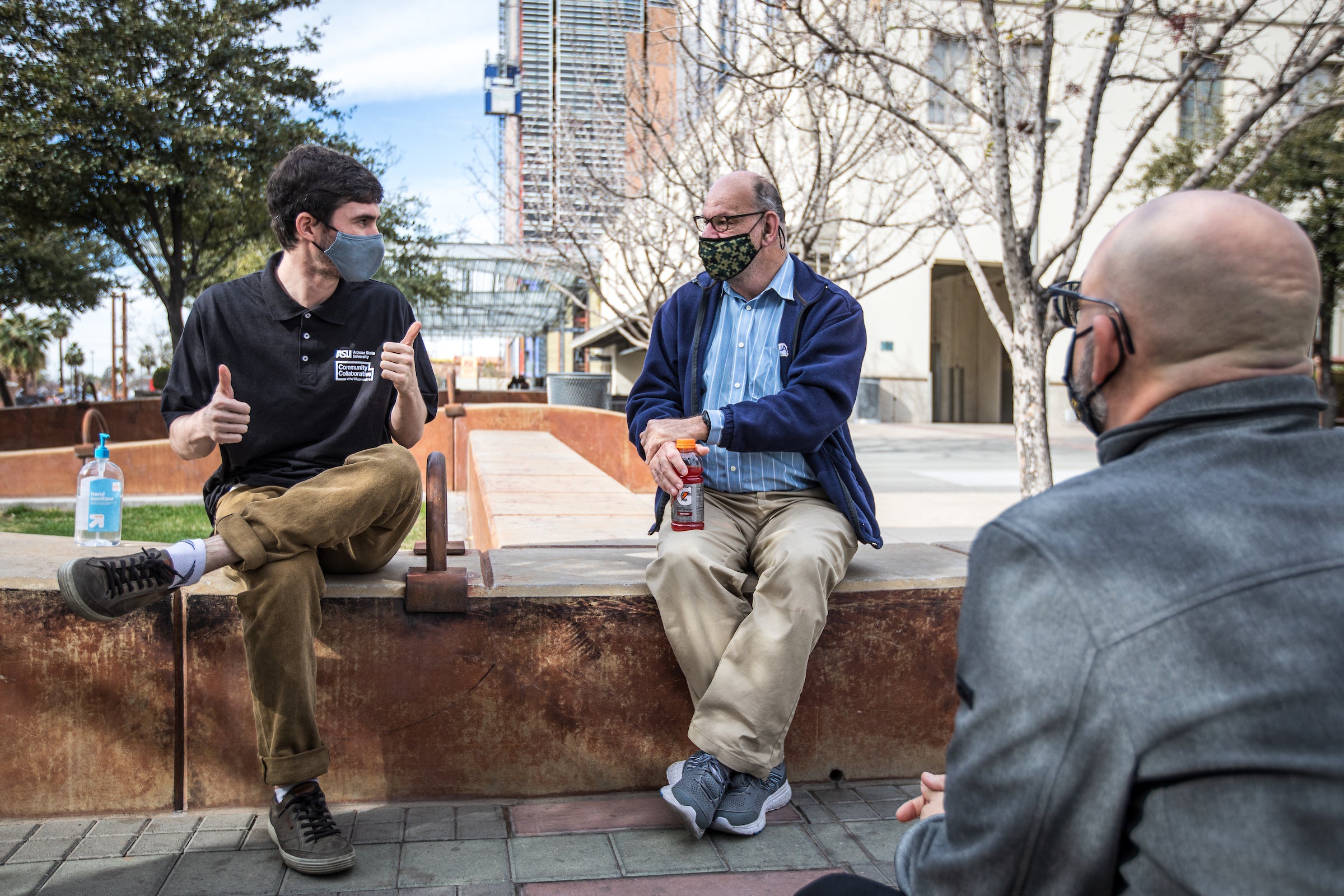 three men talking outside wearing masks