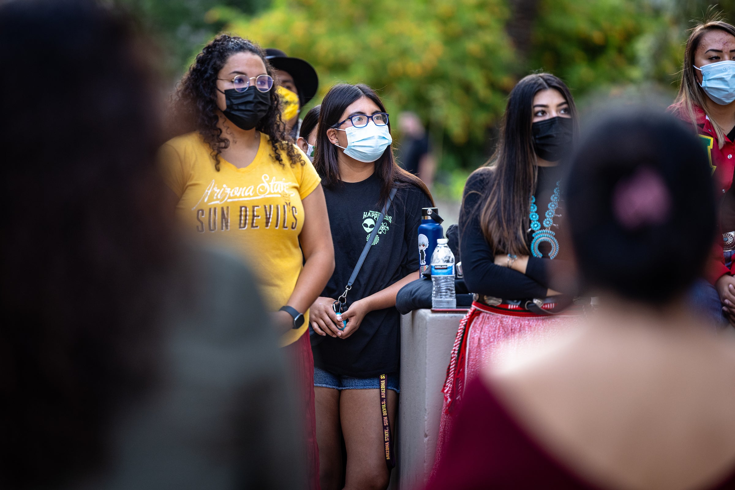 A crowd of Native American students gather outside, looking toward a stage off camera