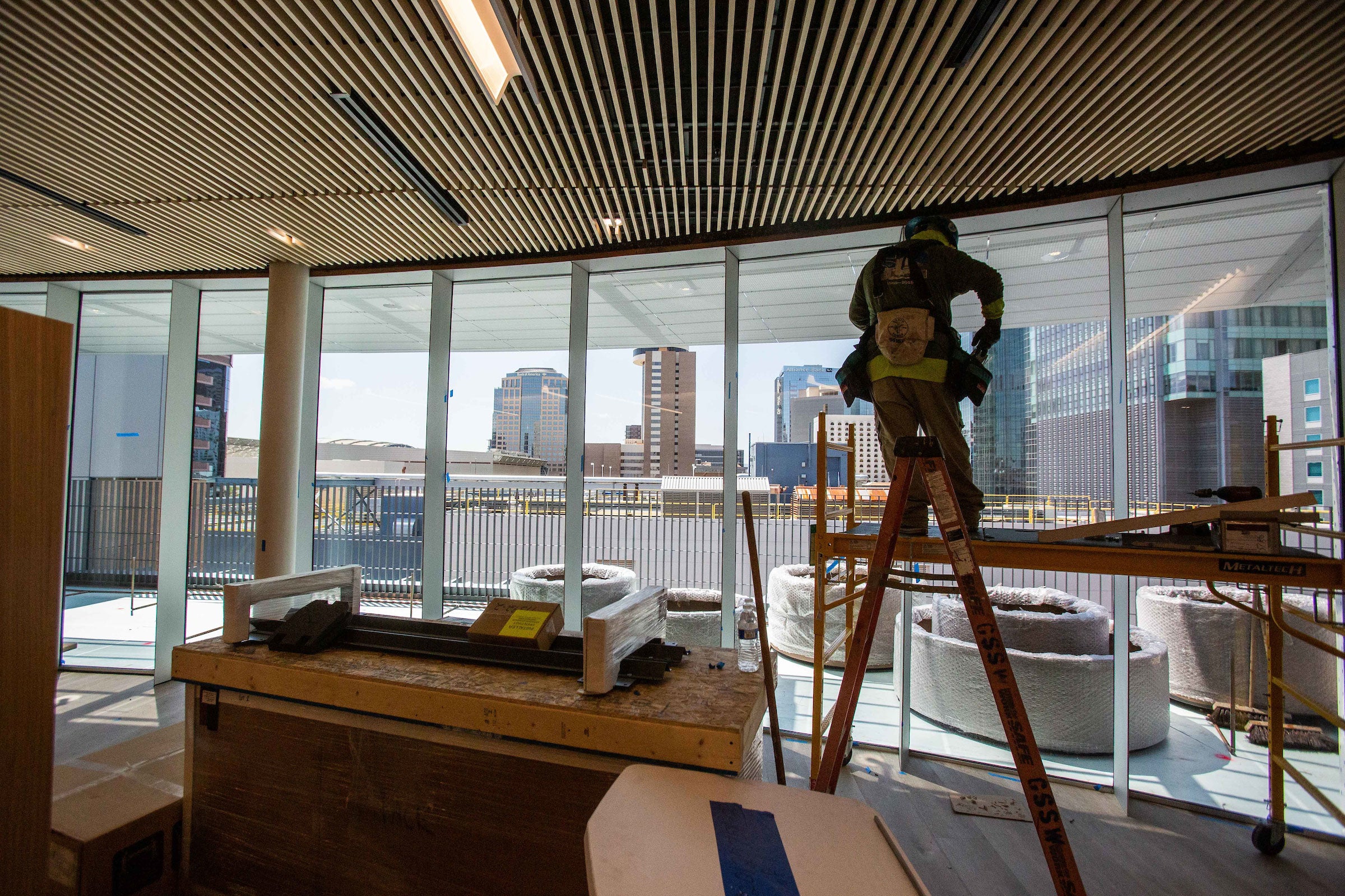 A construction worker standing on an elevated ladder platform works on the windows of a building under construction