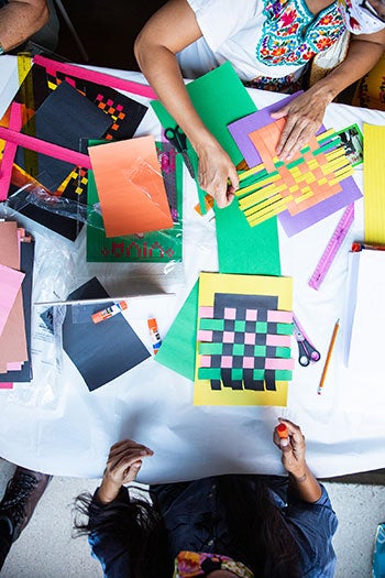 Overhead shot of people working at a table with paper weavings