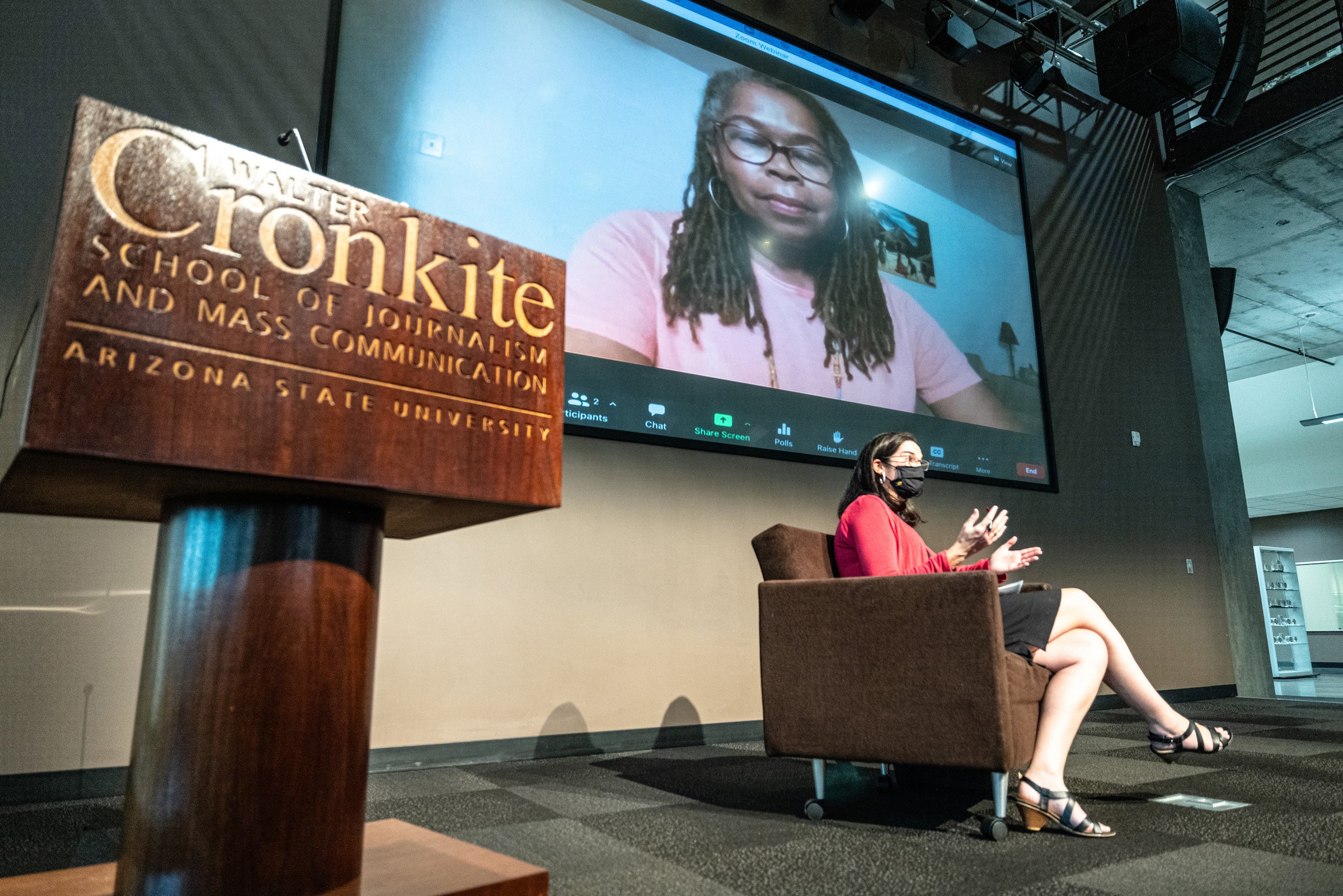 woman sitting in chair on stage with woman on projection screen behind her