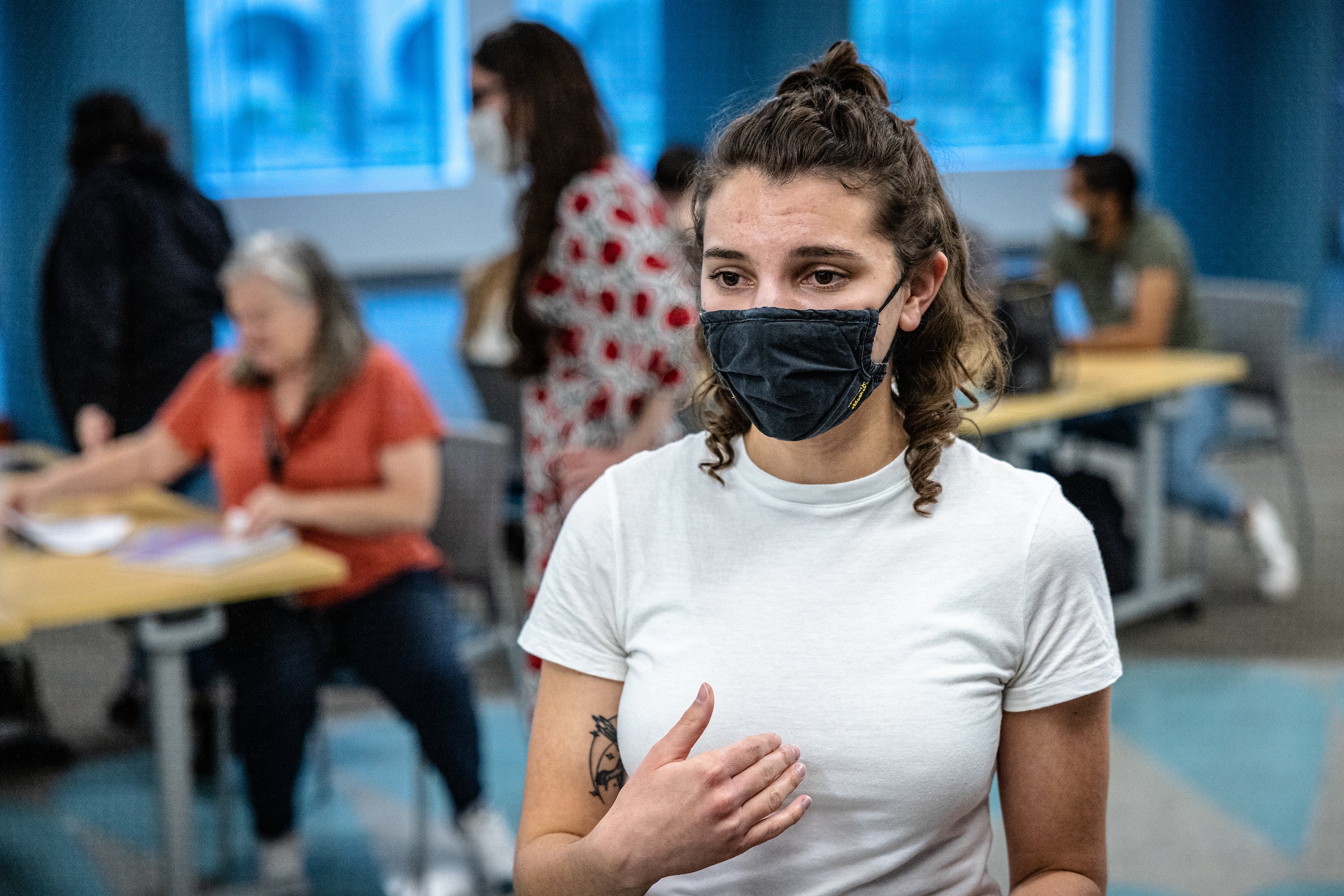 woman wearing a mask and a white t-shirt with a classroom full of students behind her