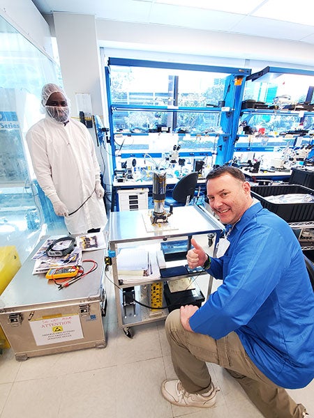 A man kneels in front of an imager camera and gives a thumbs up to the camera