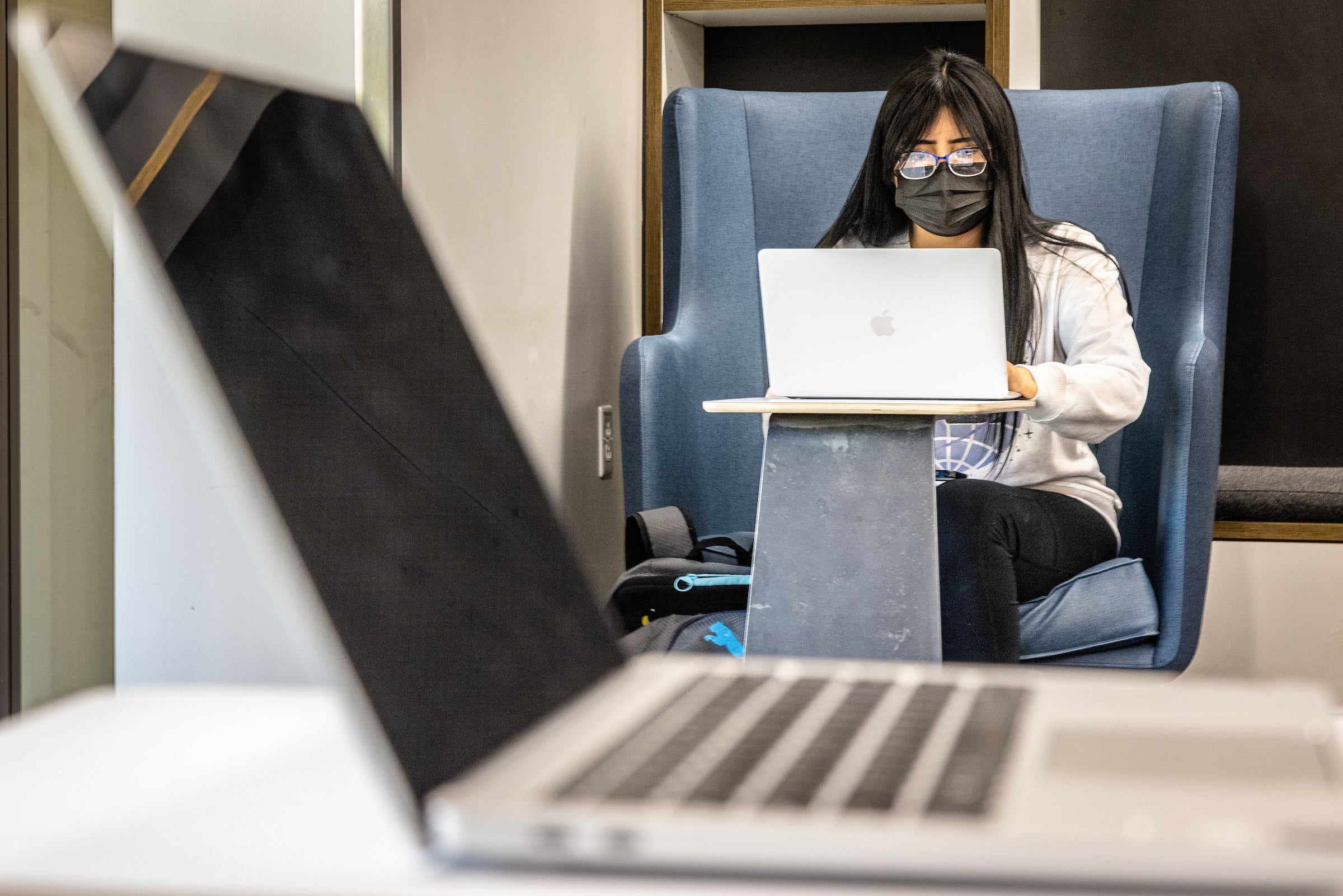 A Native American college student works on a laptop at a library; another laptop lies open in the foreground