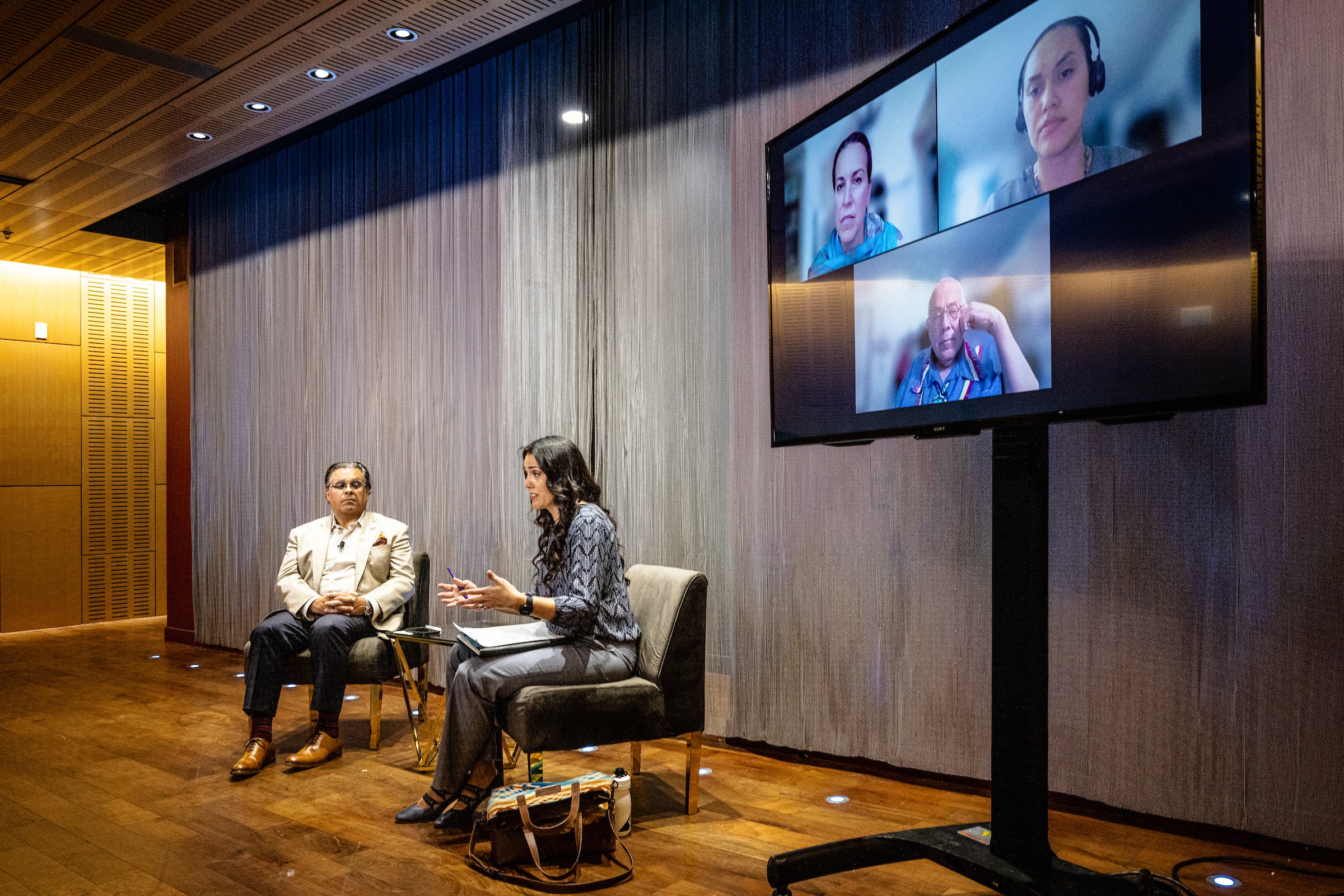 two people talking on stage at event with people joining remotely on screen