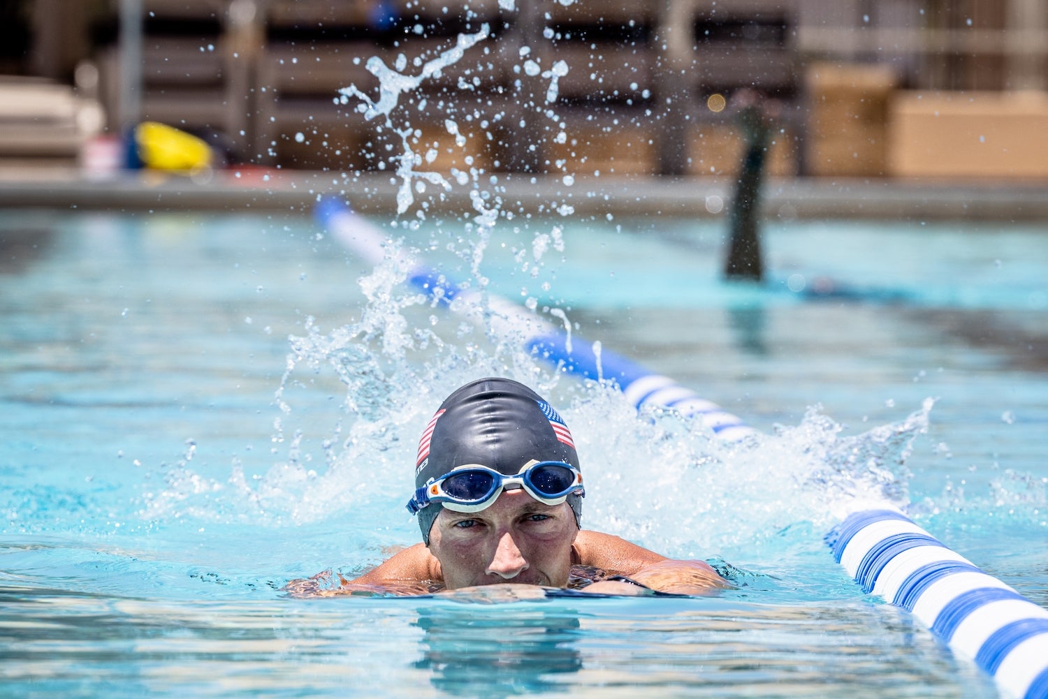 Man wearing a swim camp and goggles on his forehead in a swimming pool next to a lane marker.