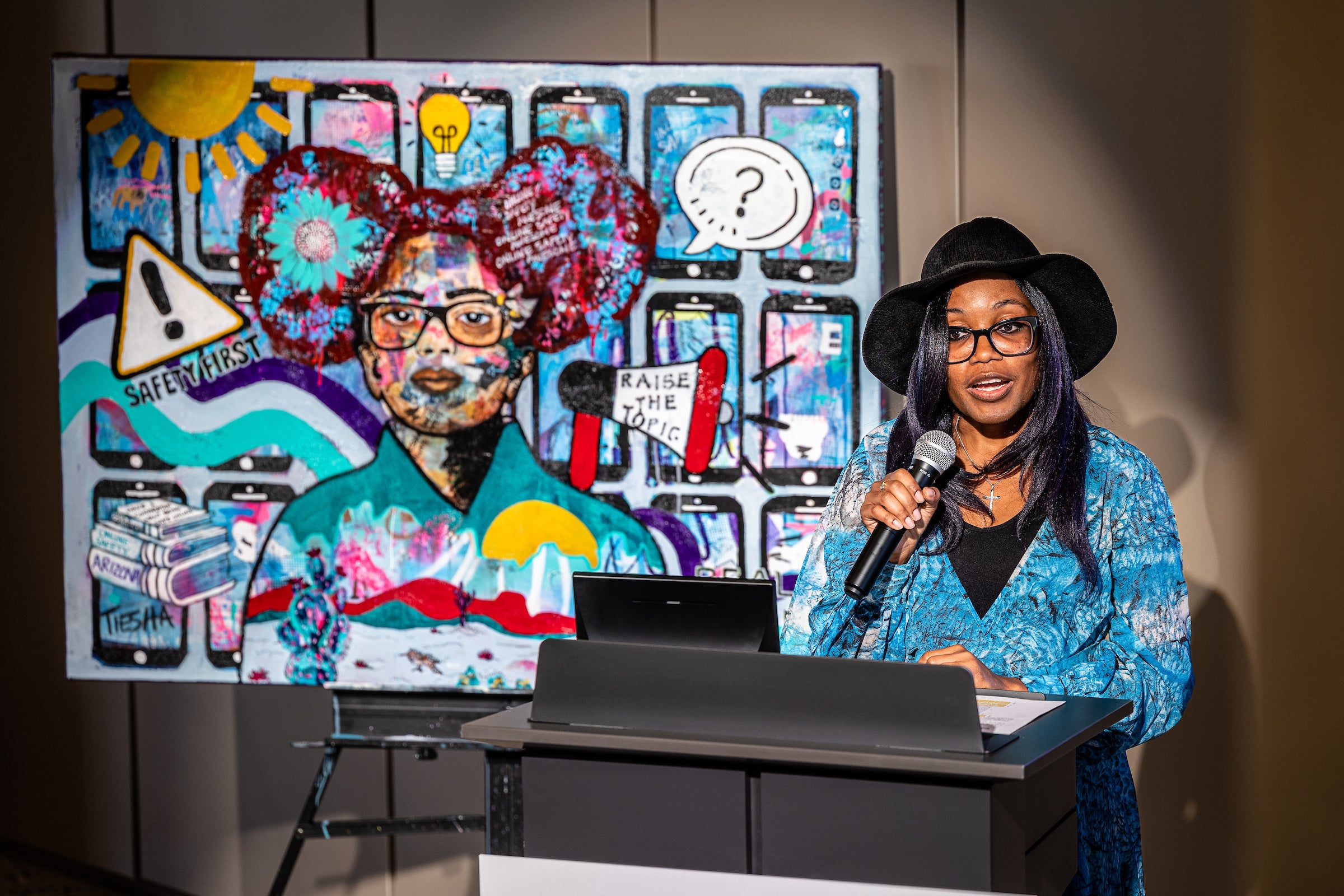 Woman speaking behind lectern in front of mural she worked on