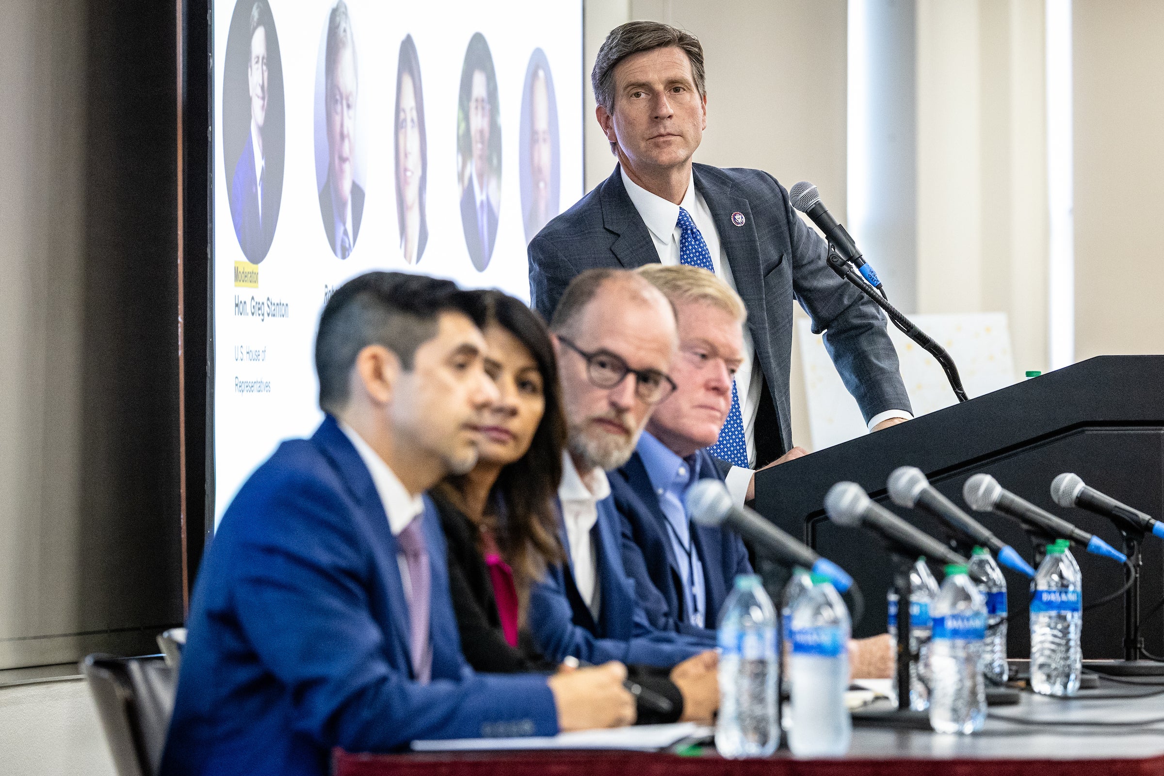 Man at lectern with group of people seated at long table next to him for panel