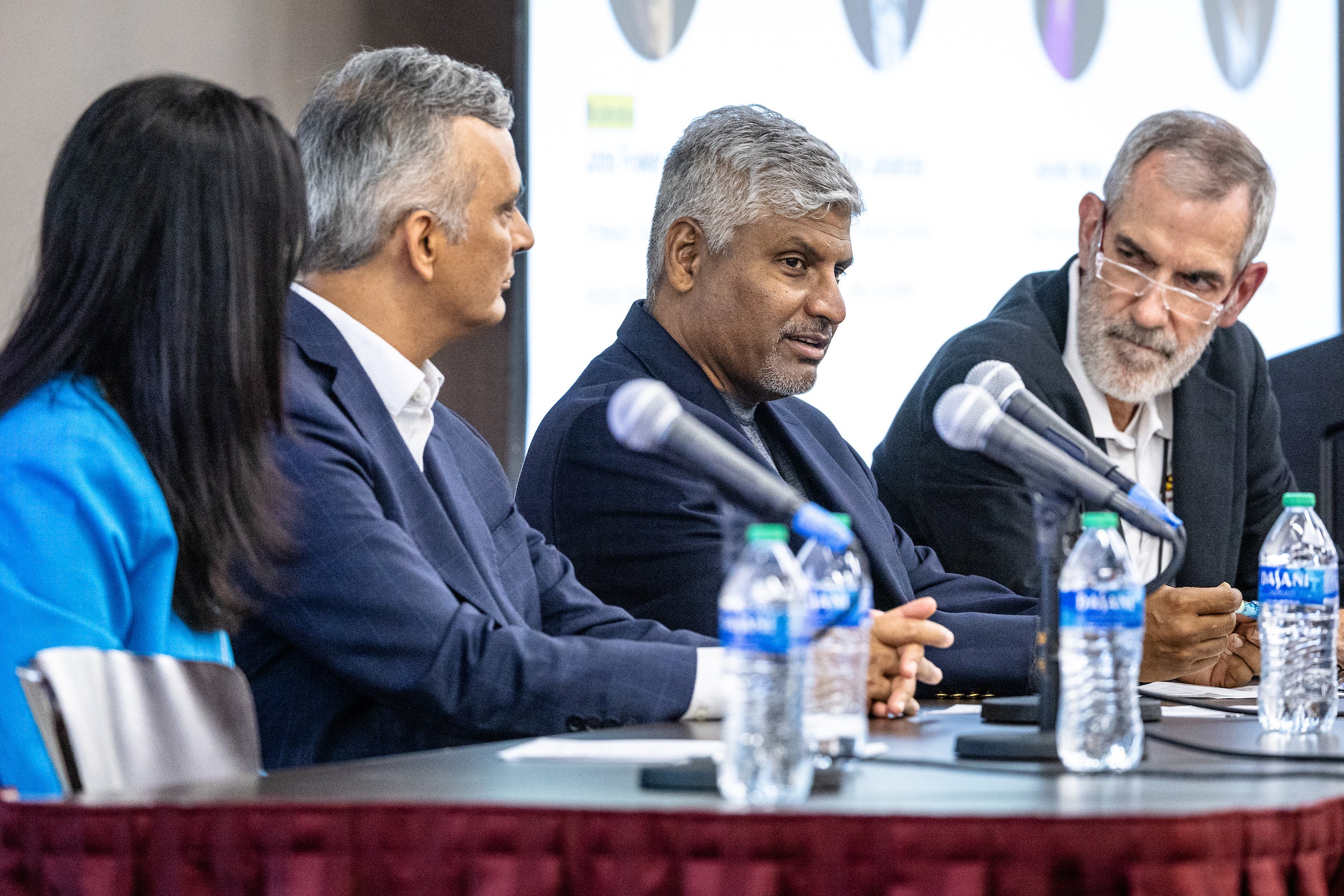 Four people sitting at long table behind microphones for panel