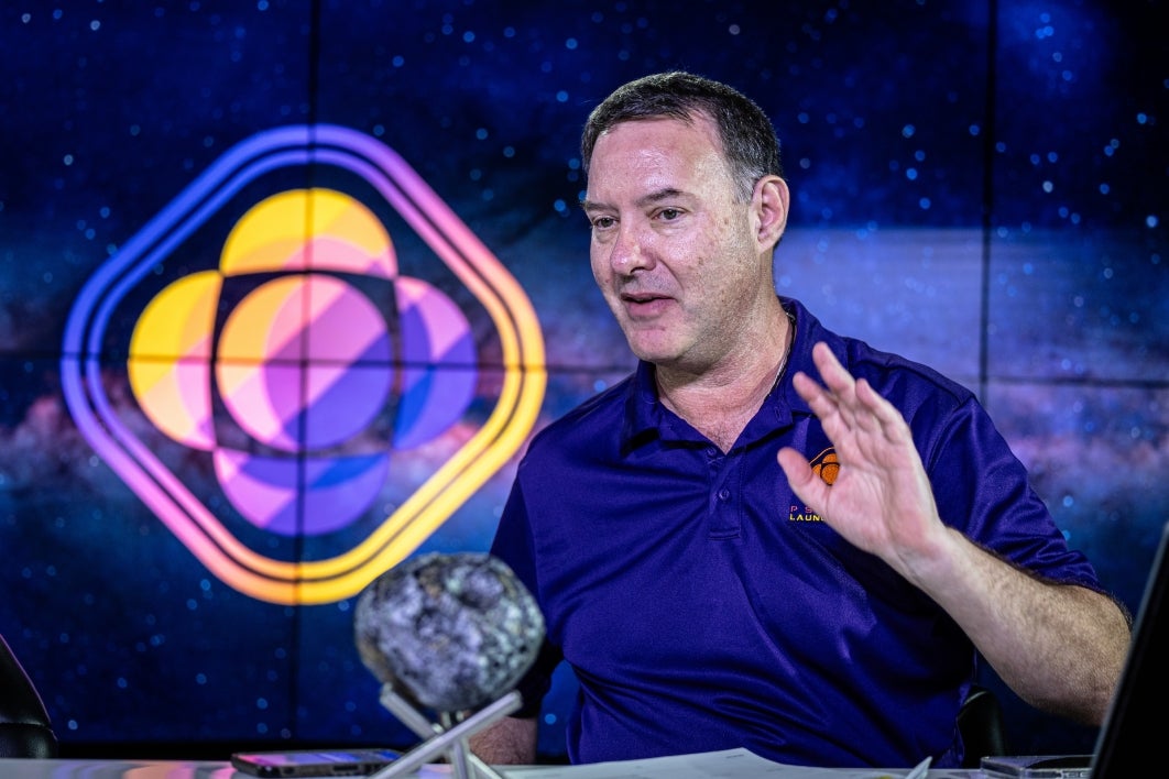 A man speaks at a table with an asteroid model on it