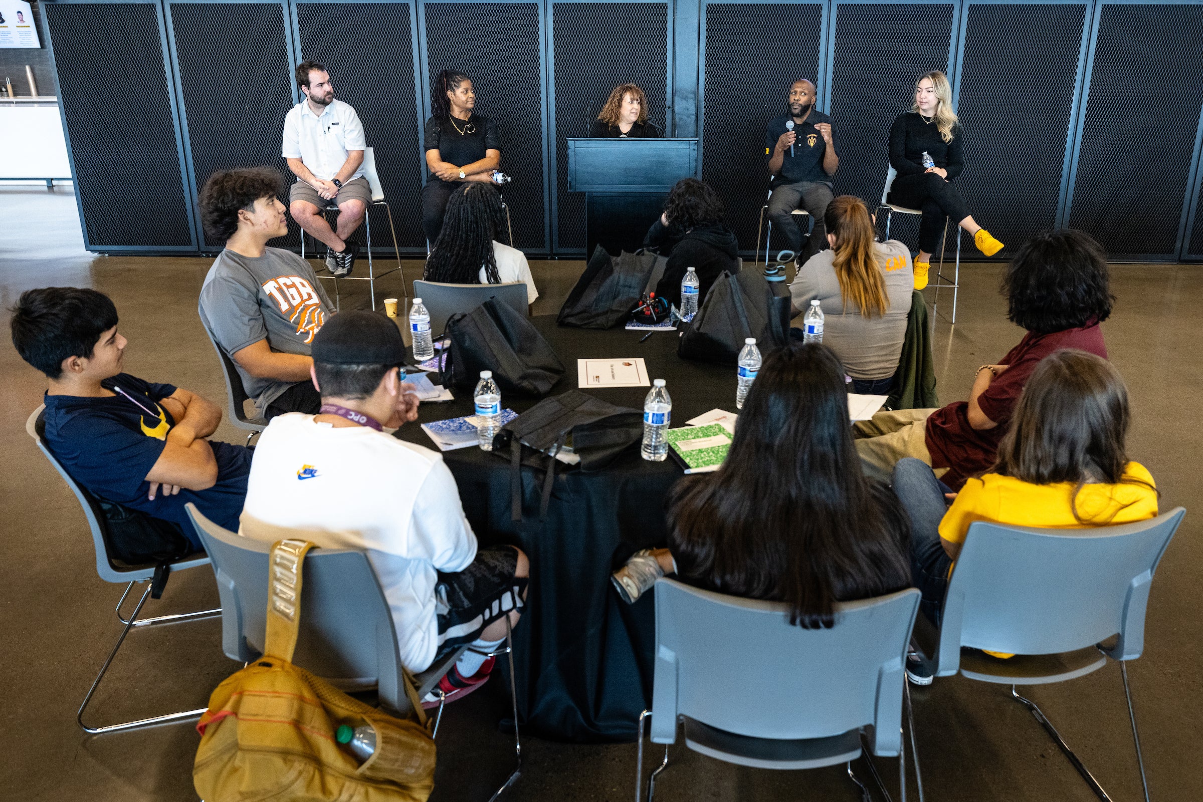 Group of high school students sitting at round table listening to five panelists