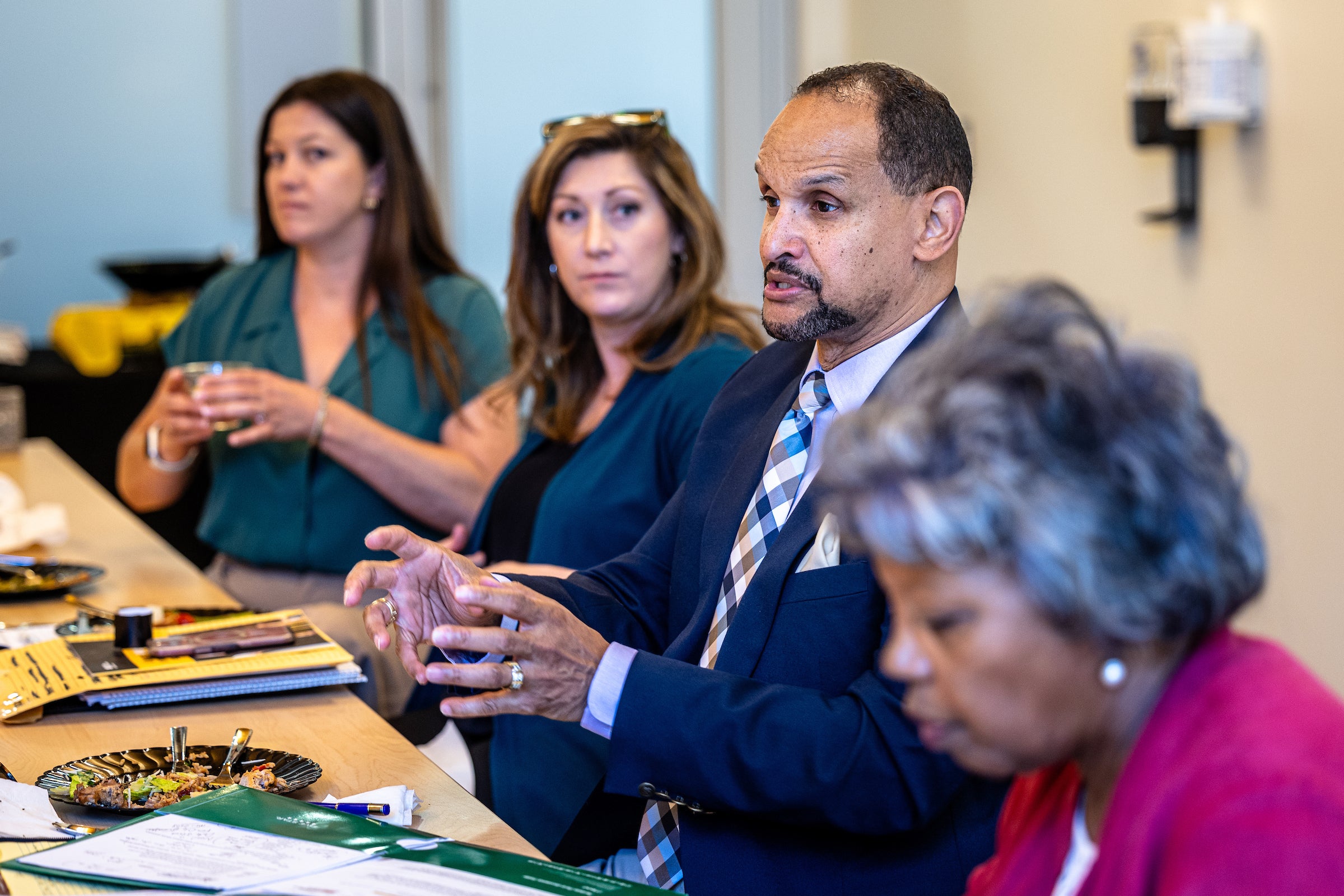 Man speaking in meeting sitting in between three other women at a table