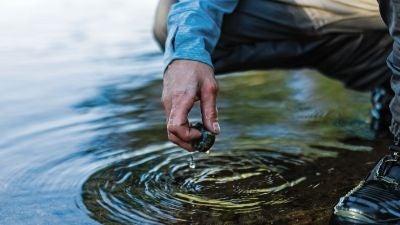 Ripples in the water after a hand pulls a rock out of the water.