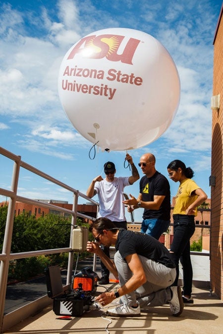 A group of four people from ASU and Axon work on camera technology and balloon on top of the Memorial Union building on the ASU Tempe campus.