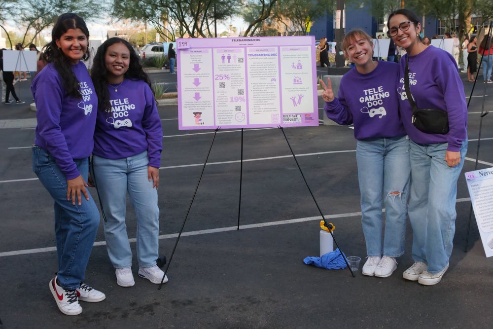 A team stands on either side of their winning poster. They are all wearing purple sweaters that say telegaming doc on them