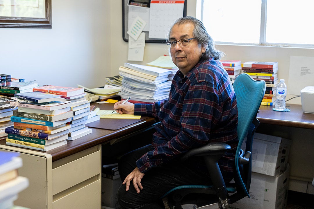 David Martinez sits in his office, surrounded by stacks of books. 