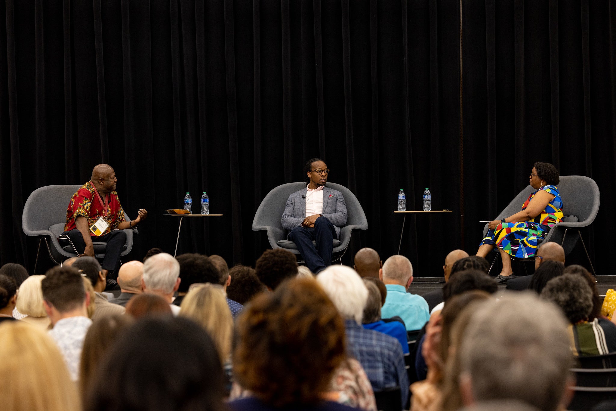 Three people sitting and talking on stage in front of a large crowd