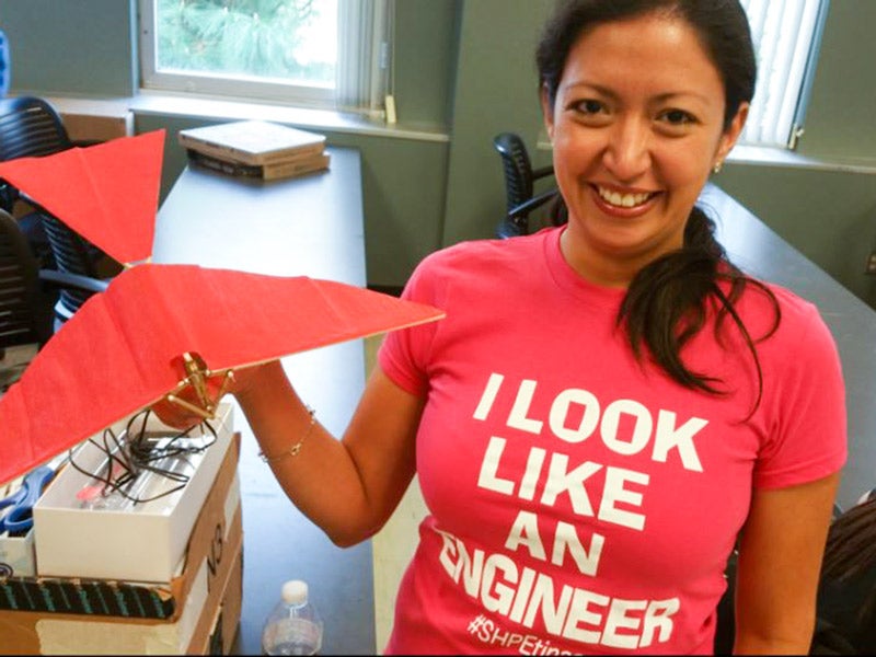 An engineering student holds a bird made of paper and balsa wood.