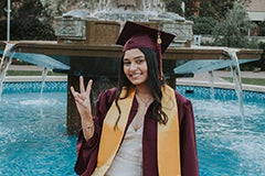 woman in cap and gown posing in front of water fountain