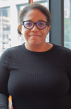 portrait of new ASU faculty member Brandi Adams, wearing glasses, a black shirt and smiling