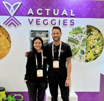 ASU alum Alex Swartz standing next to a woman with his arm around her. Behidn them is a sign that reads "Actualy Veggies."