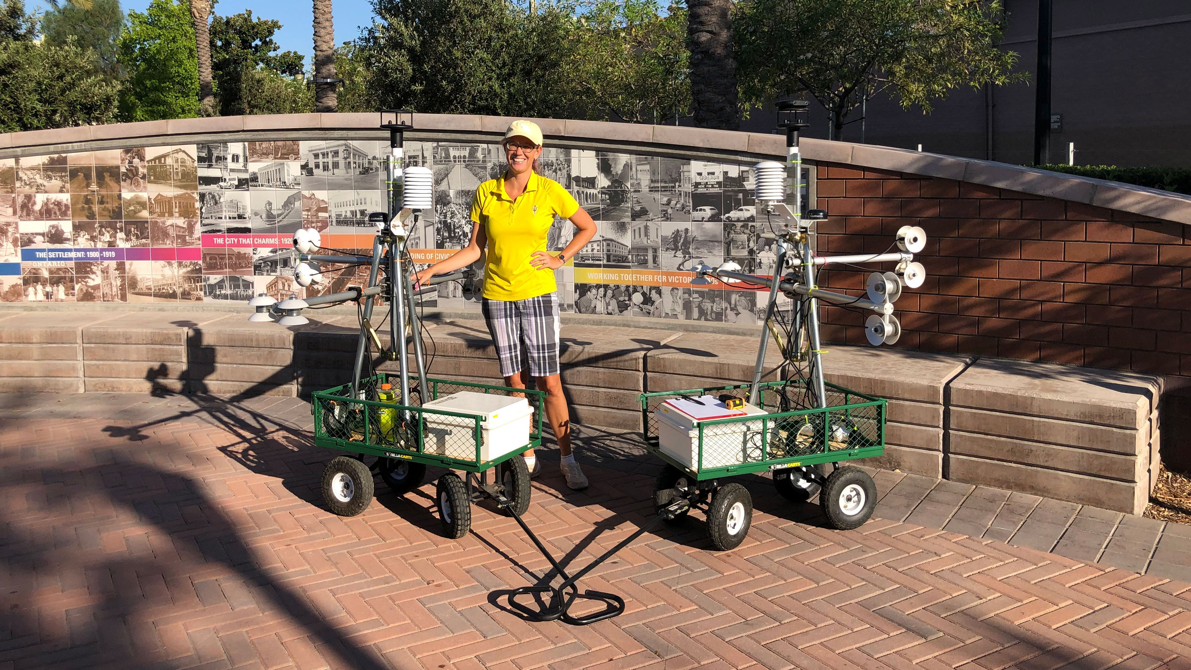 A woman poses with two carts full of instruments for measuring shade and temperatures