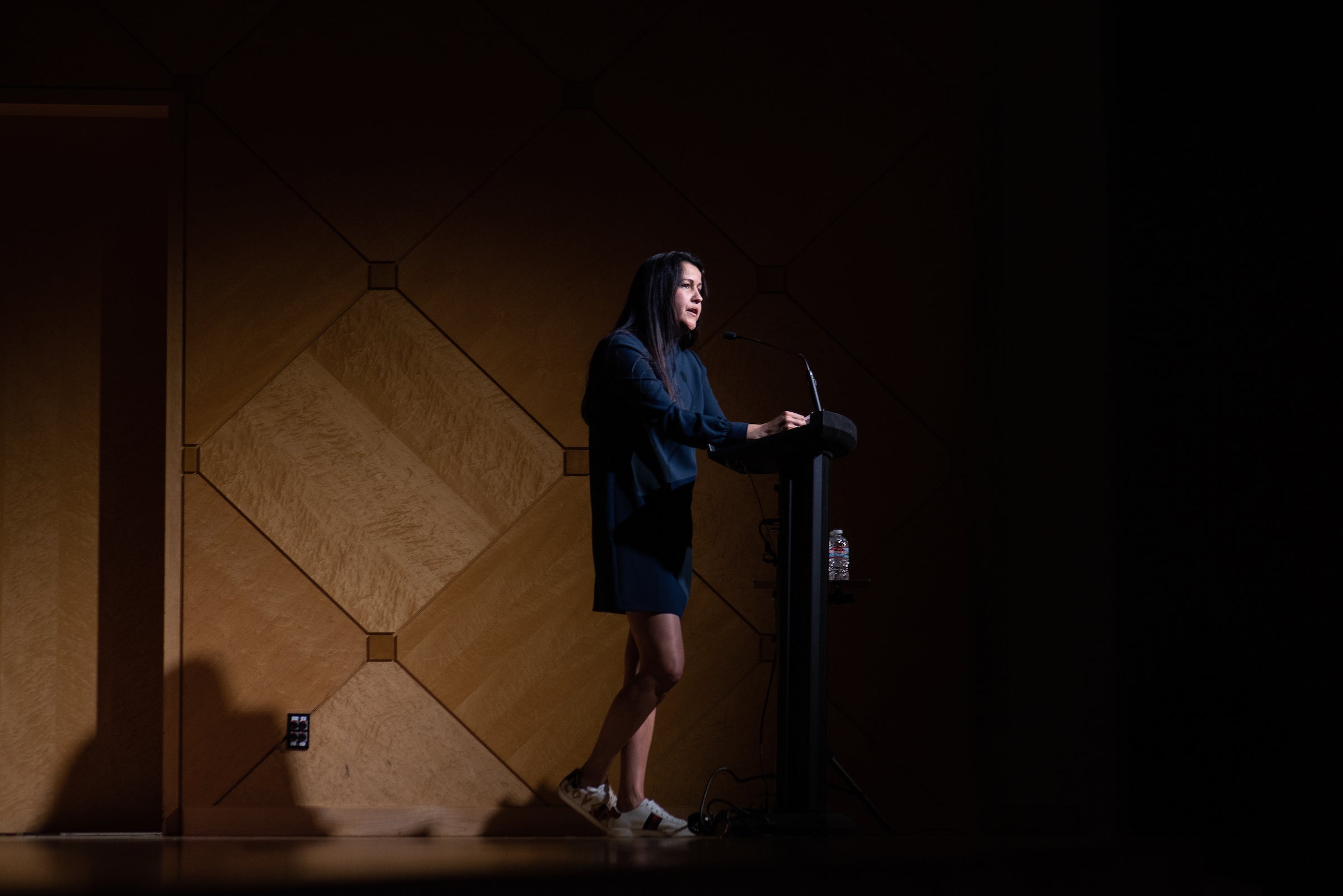 woman speaking on stage, behind a lecturn, to an audience