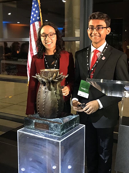 Two college students stand behind a trophy after winning the 2019 inaugural Regents Cup debate tournament