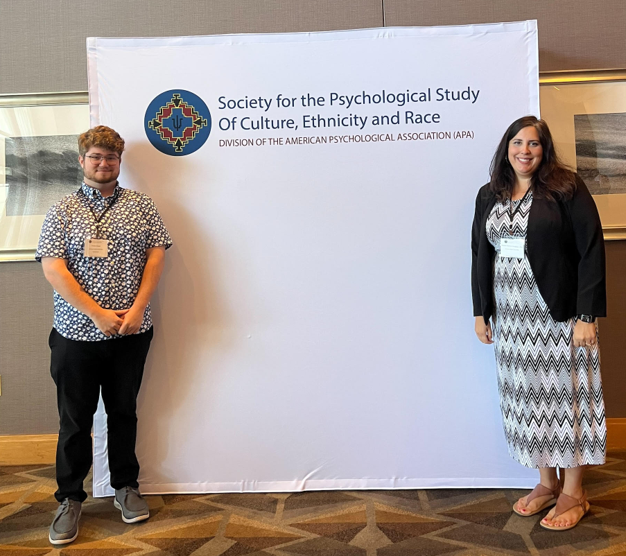 People standing next to a sign that reads "Society for the Psychological Study of Culture, Ethnicity and Race."