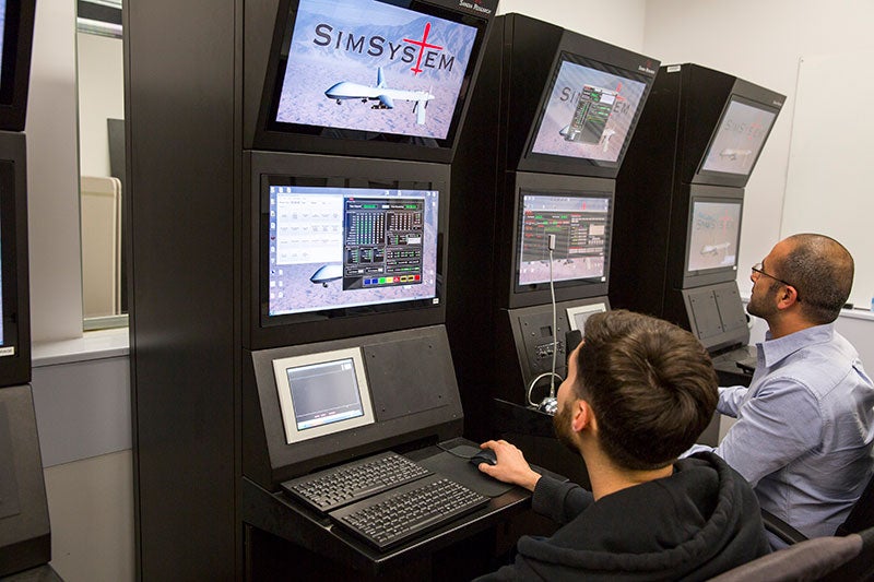 Two men operate a drone simulator in a lab. The caption reads: Mustafa Demir (left) and Aaron Bradbury fly a drone with assistance from a synthetic teammate in Nancy Cooke's lab. Photo courtesy of the Ira A. Fulton Schools of Engineering.