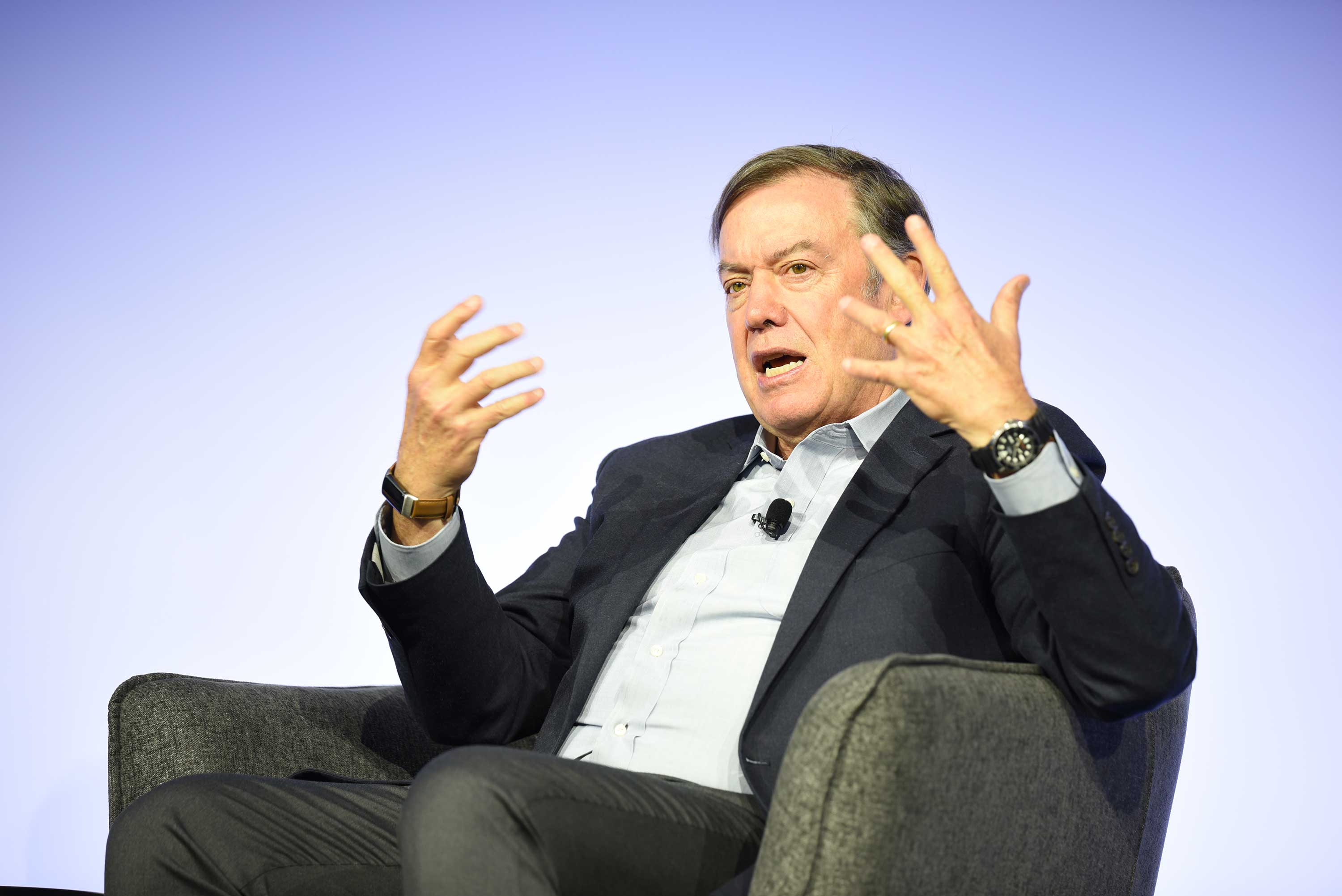 man sitting in chair on stage speaking to audience