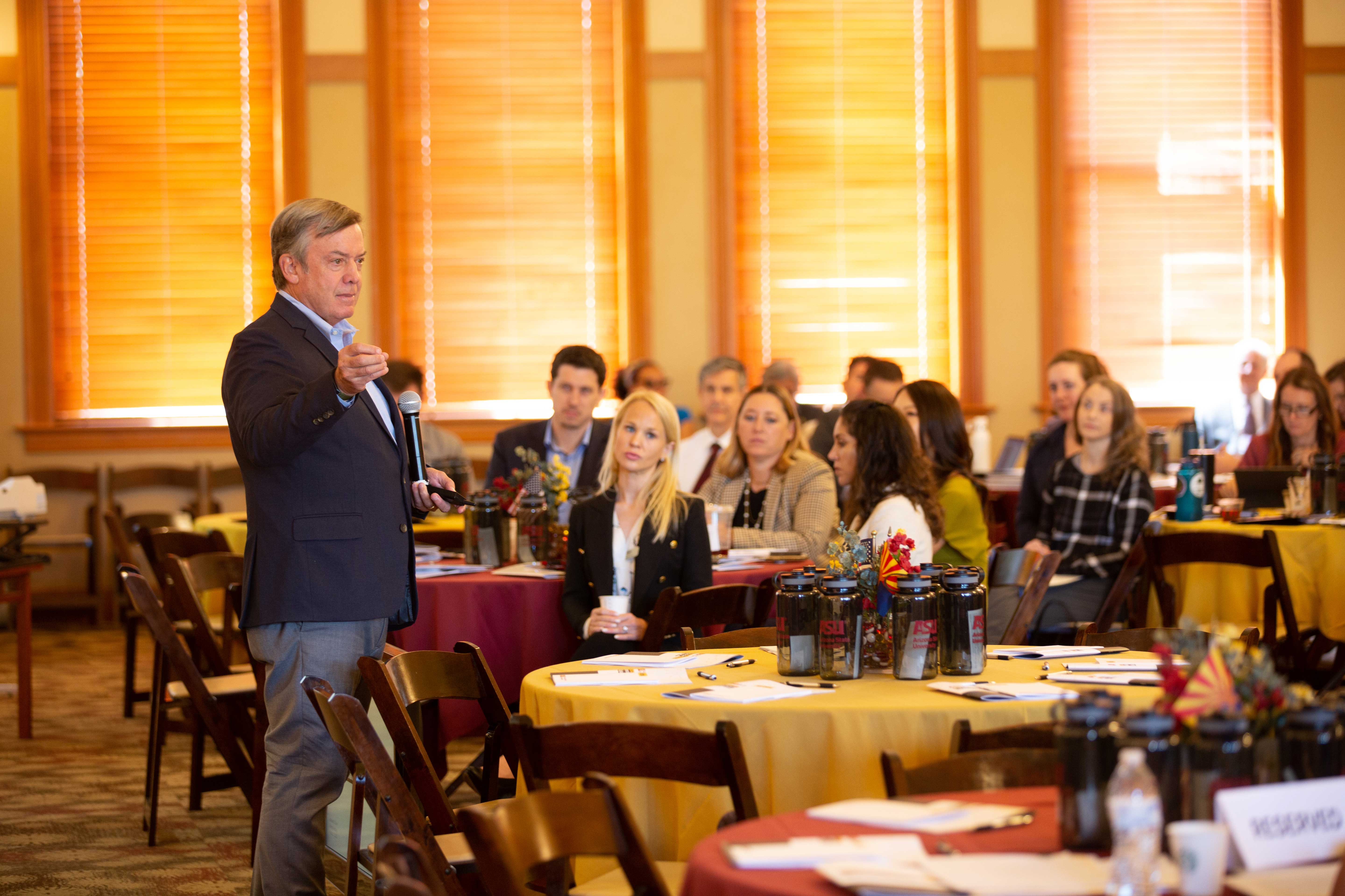 ASU President Crow speaking to group of people seated at round tables