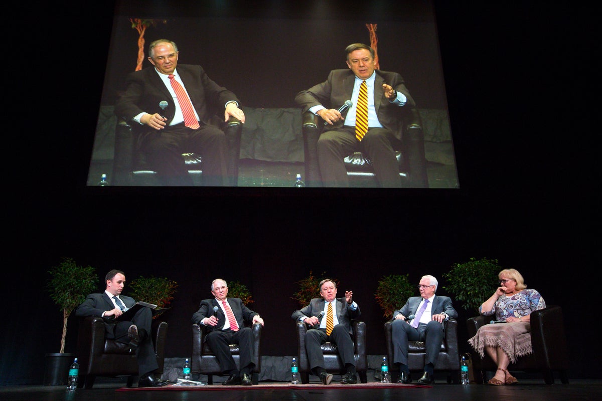 People sitting on a stage, under a projection screen.