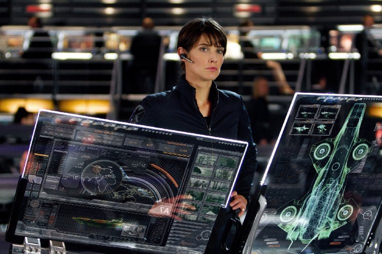 A woman stands at a military control panel.