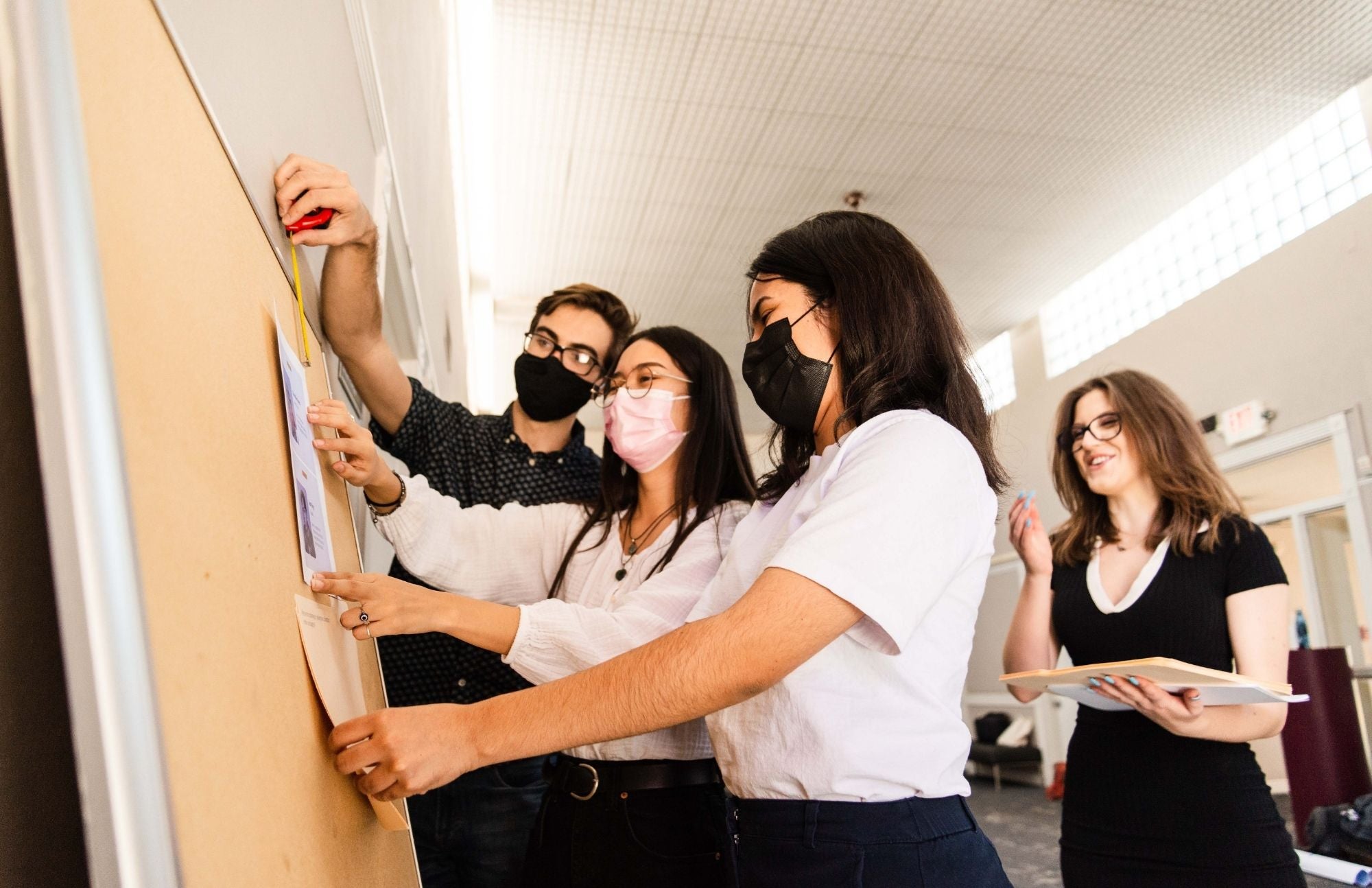 Students gather in front of a cork board to pin flyers to it.