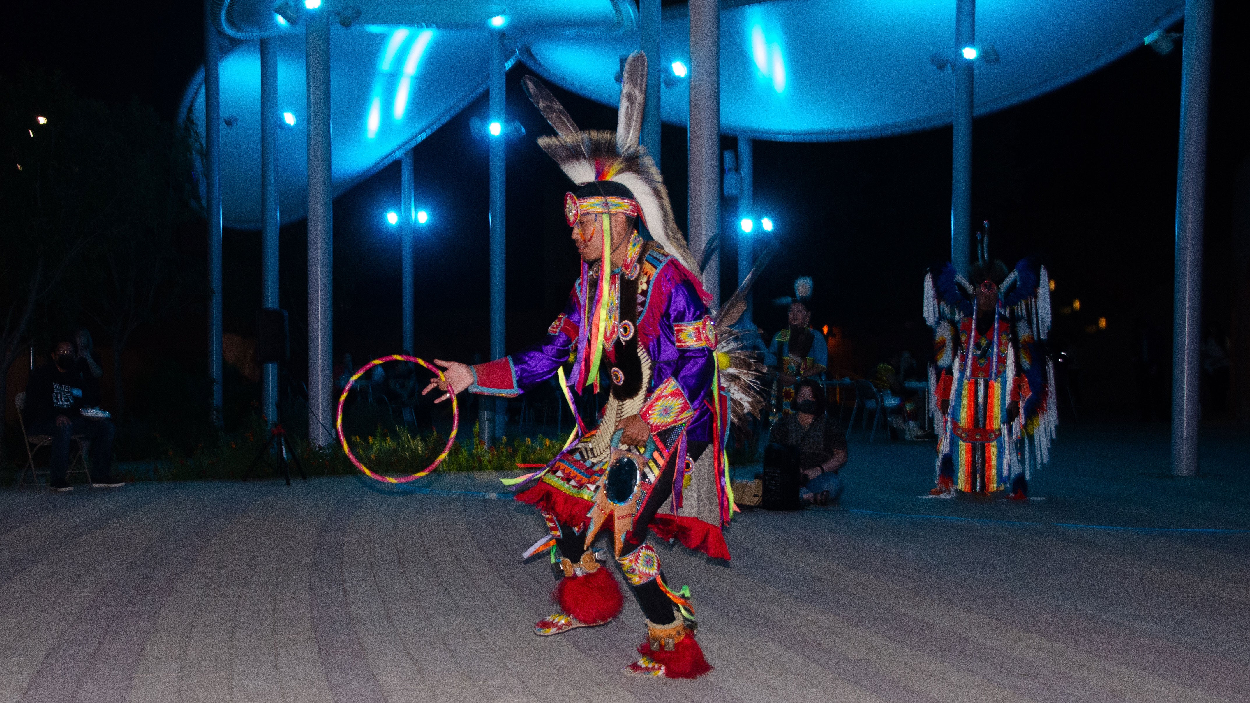 A Native American dancer in full regalia performs on an outdoor stage