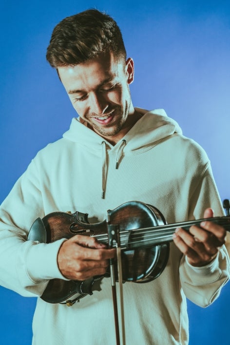  holding a violin and smiling against a blue background.