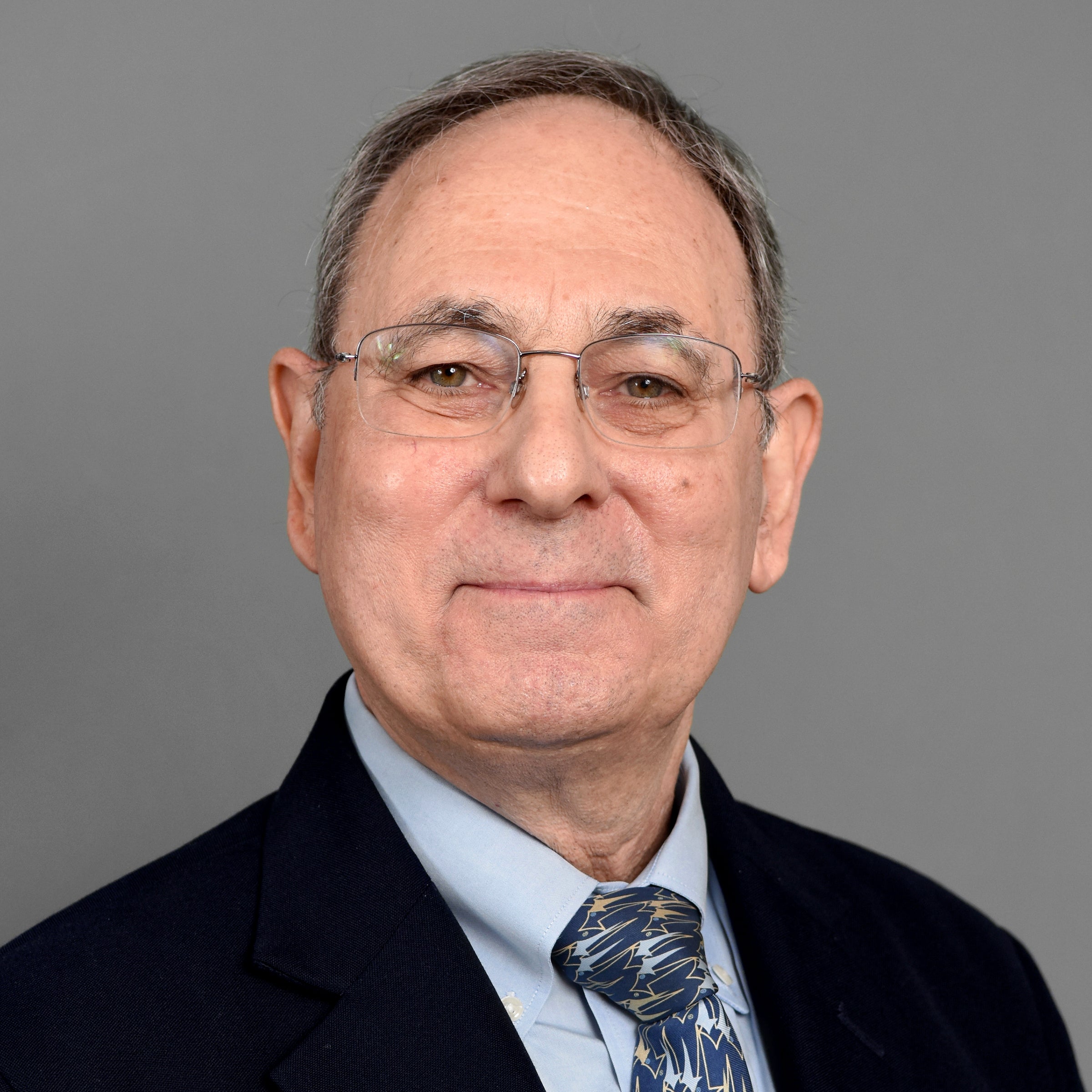 Geoffrey Gonsher wearing dark blue suit, with bluch graphic tie and glasses)