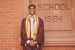 Man standing in front of old main in cap and gown