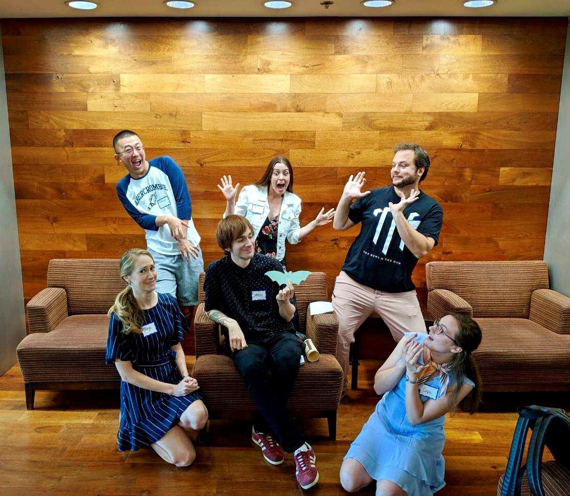 Bosnian/Croatian/Serbian instructor Jakov Causevic poses with his students in 2019. Three are sitting and three are standing, all in front of a light brown wood plank wall.