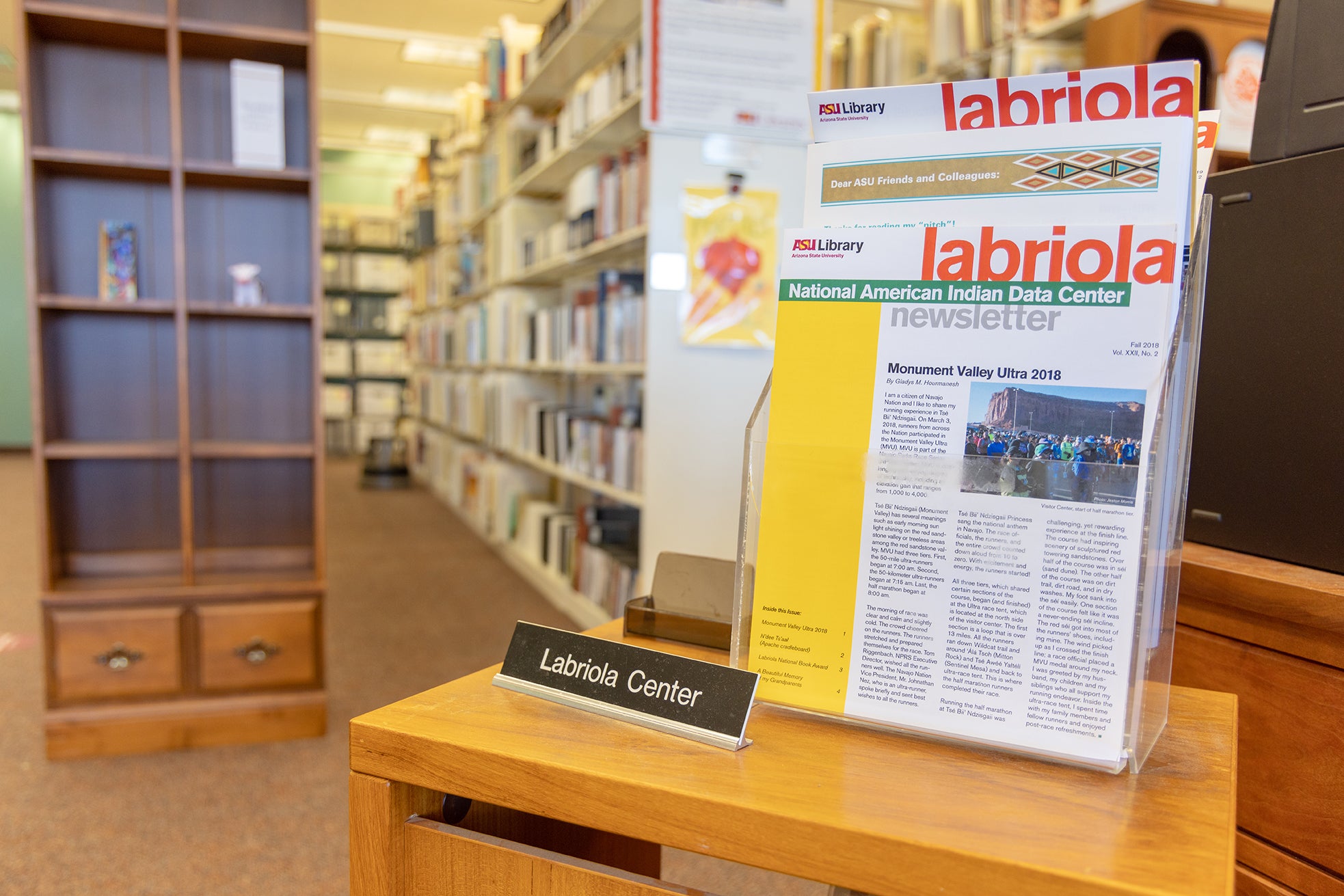 Newsletters displayed in a holder on a small table with bookshelves and stacks in the background