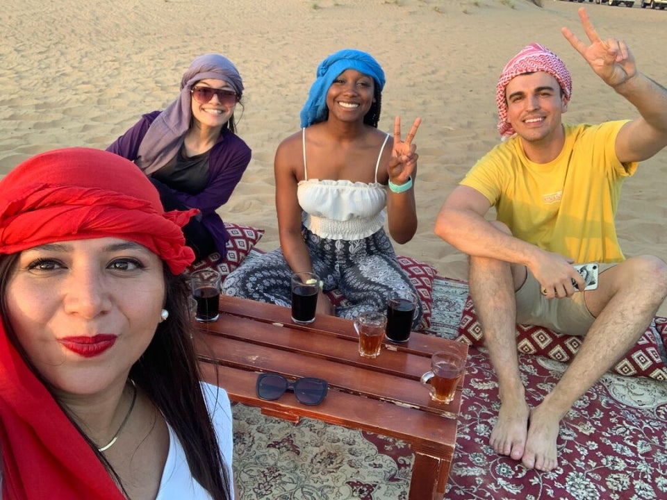 People sitting on a beach with drinks and smiling at a camera.