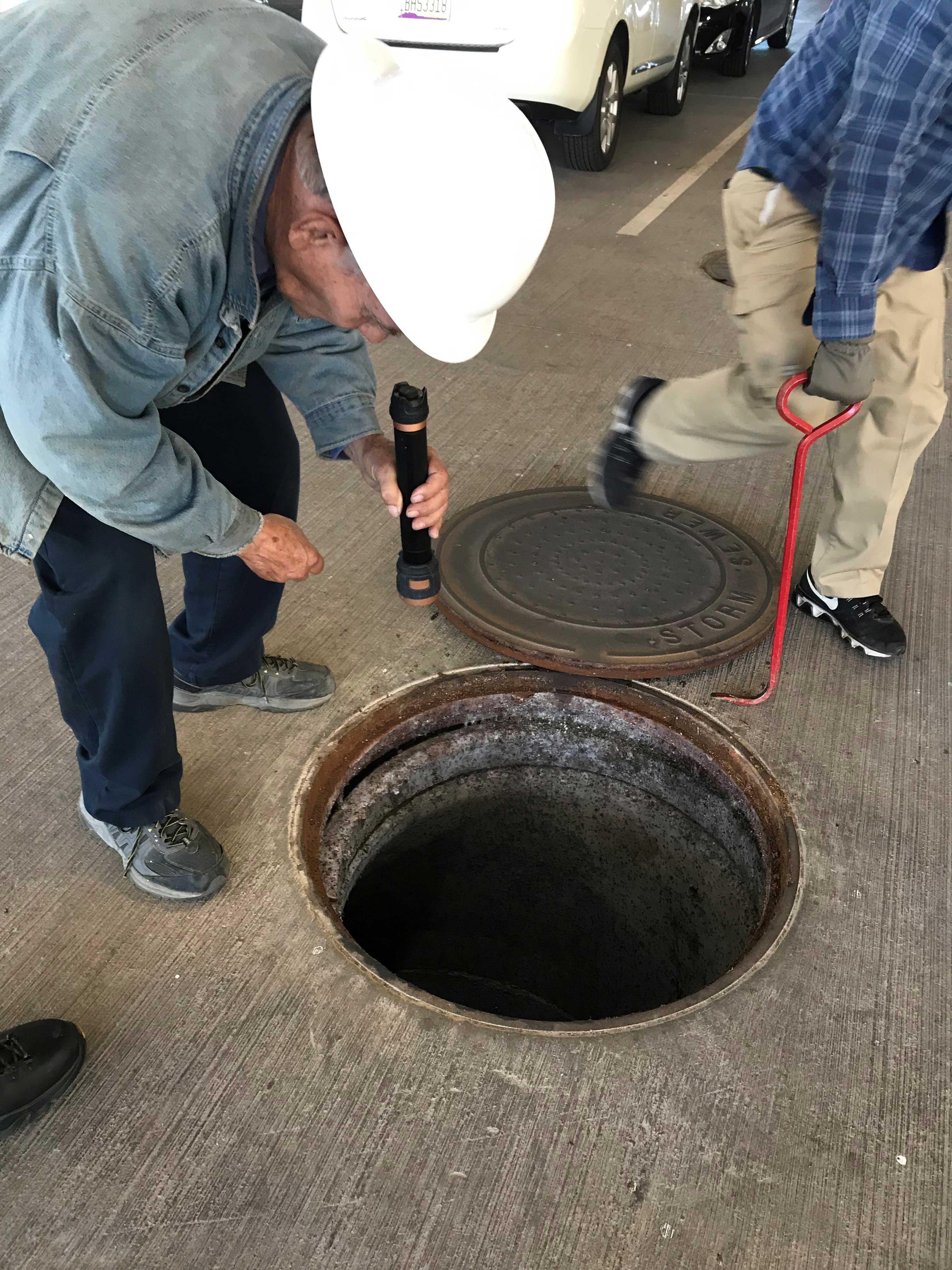 Man peers down drywell with flashlight