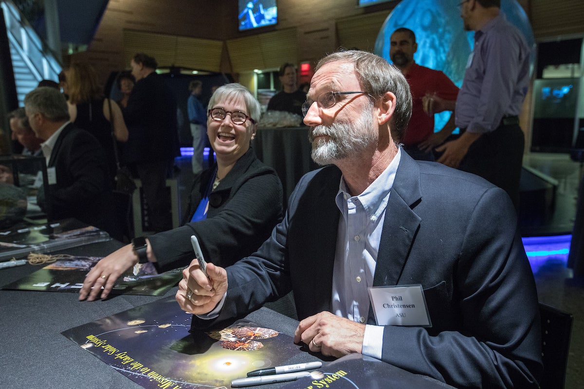 two people at tables signing posters